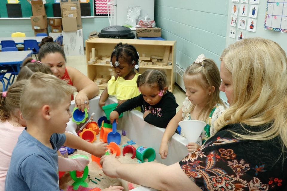 Adults and children playing with sand and toys in a sensory bin
