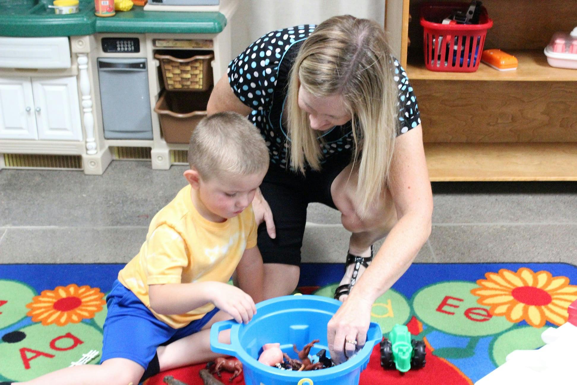 Adult and child playing with toys in a blue bucket on a colorful rug