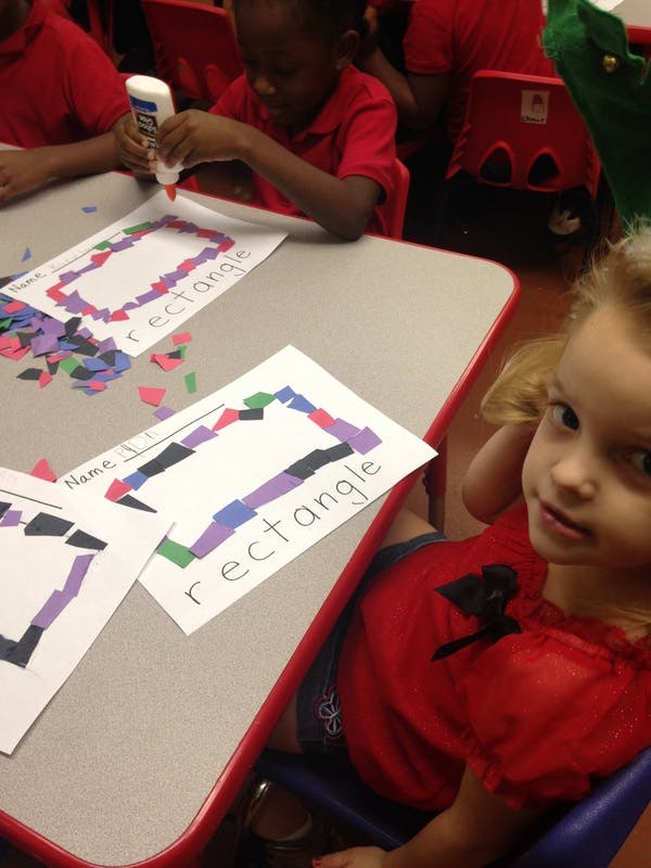 Child gluing paper pieces onto a rectangle outline