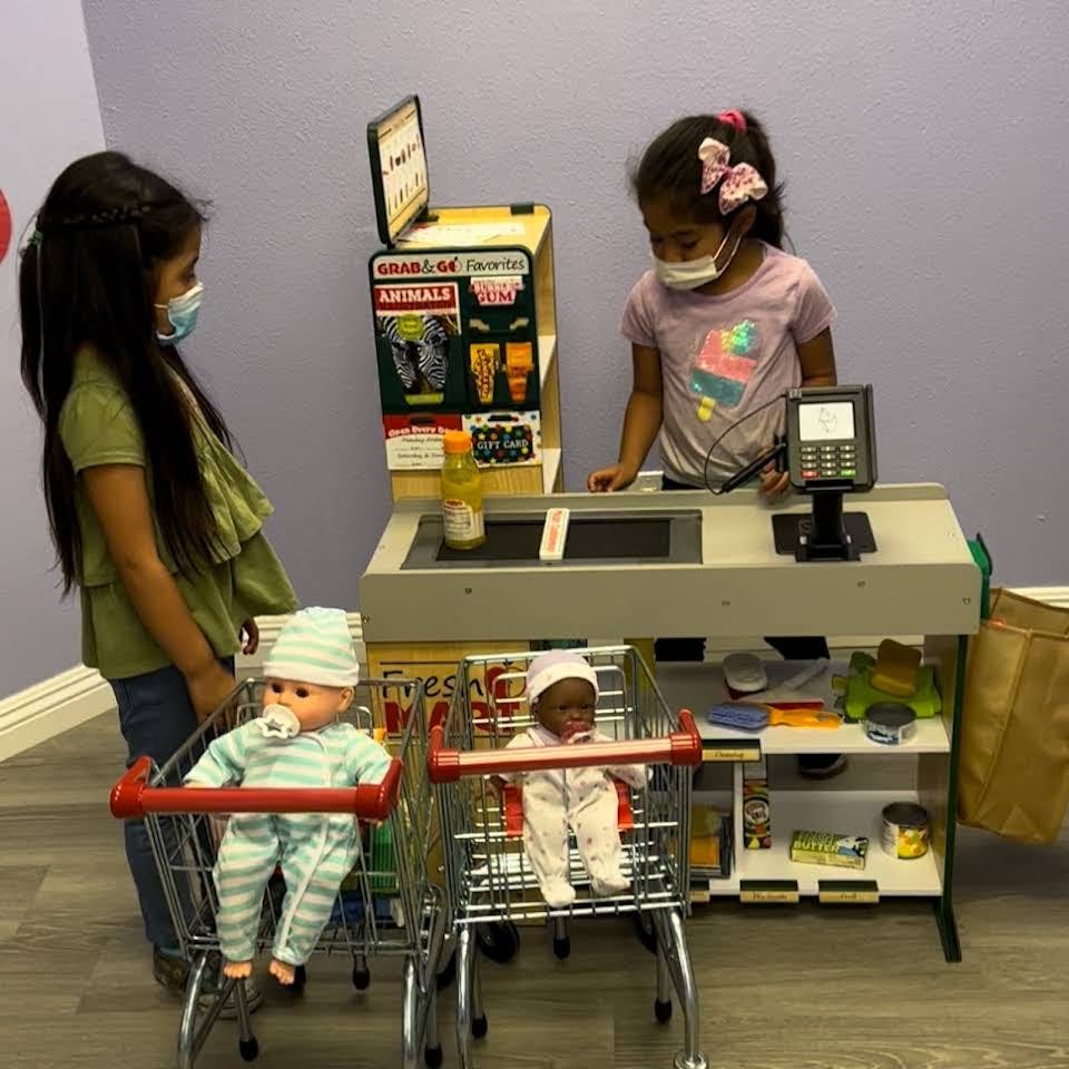 Two children playing with a toy checkout counter and shopping carts with dolls