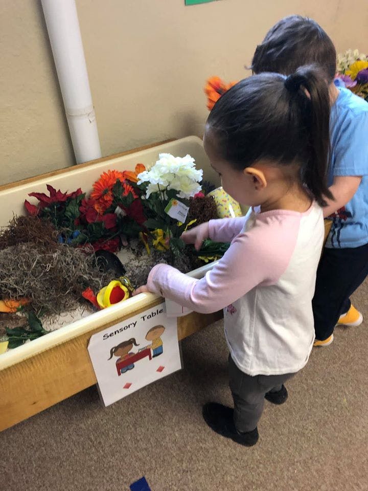 Child playing at a sensory table with another child in the background