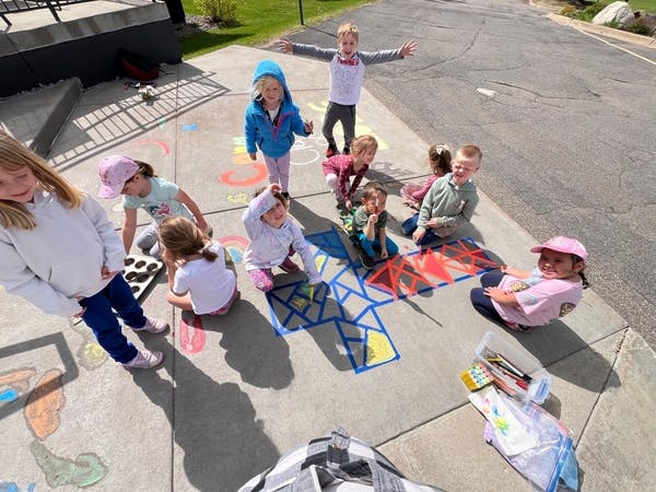 Group of children playing with chalk and tape on a paved surface