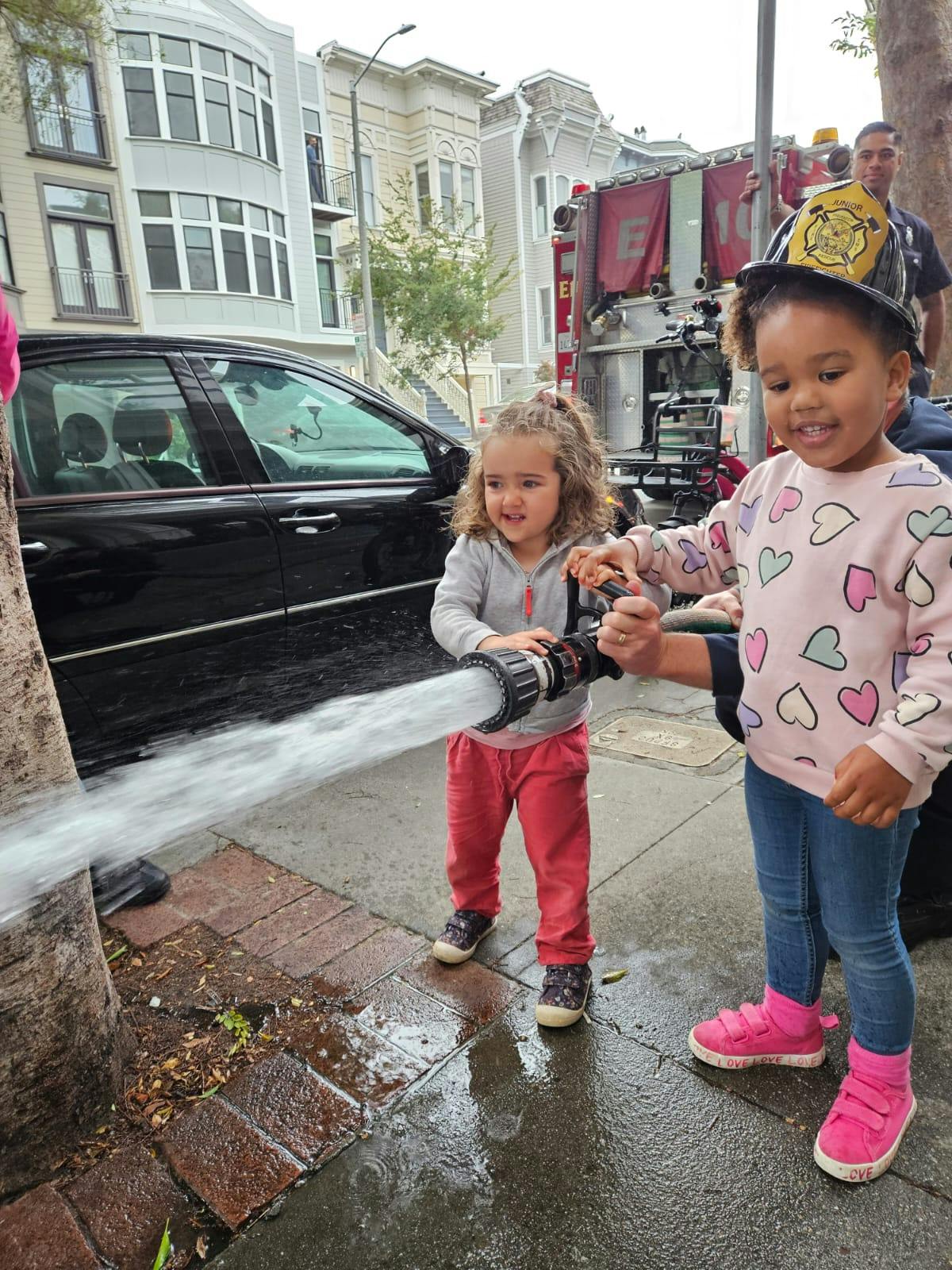 Two children holding a fire hose, spraying water