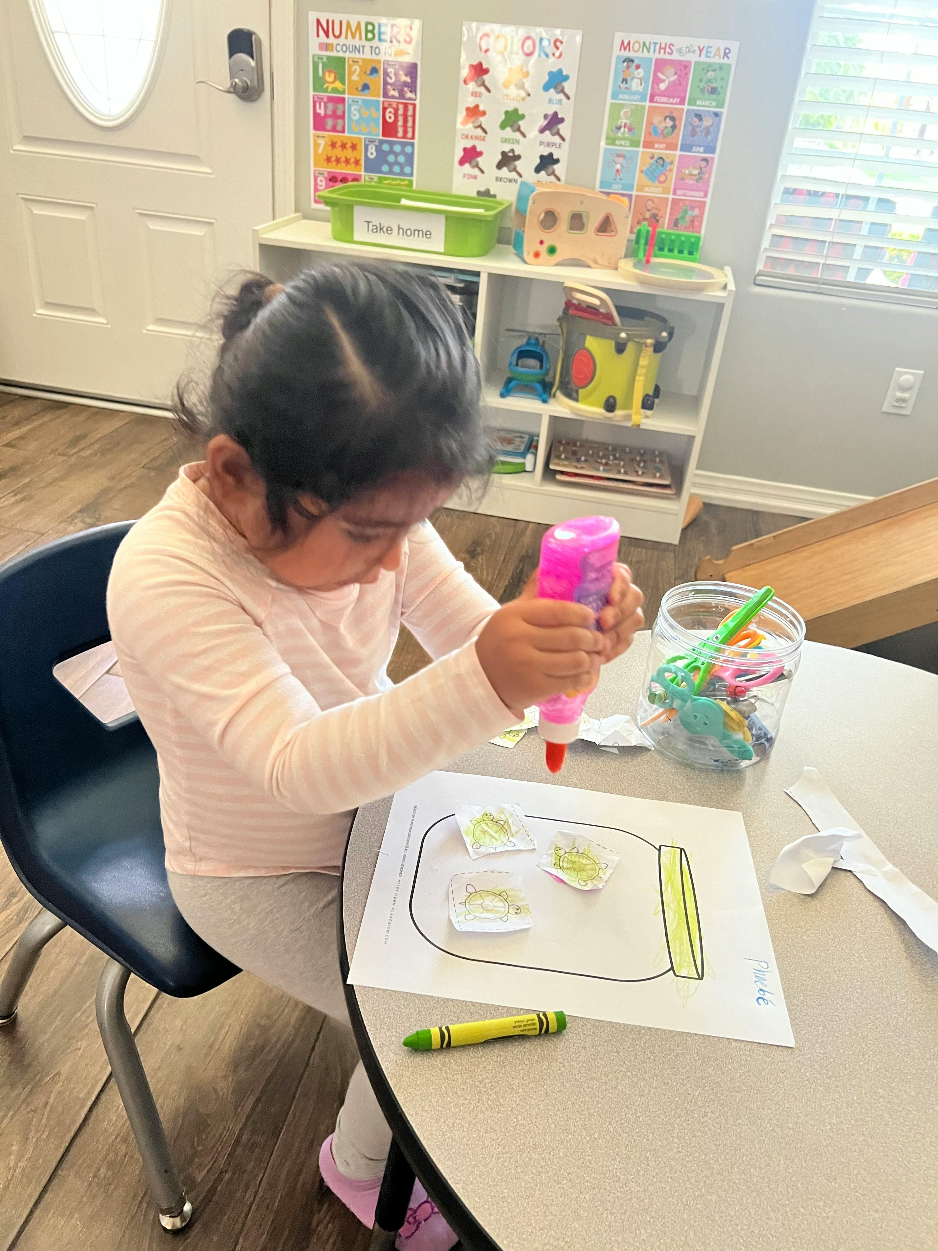 Child squeezing glue onto paper with a drawing of a jar