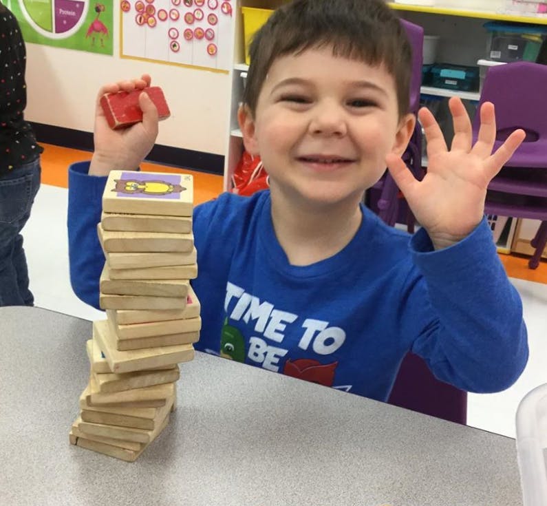 Child playing with wooden blocks, holding one block and waving