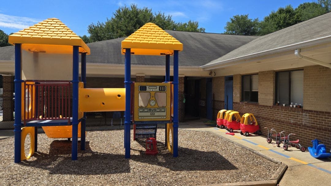 Playground with yellow and blue play structure, ride-on toys, and building
