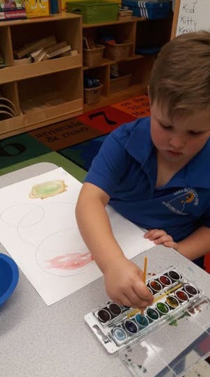 Child painting with watercolors at a table in a classroom