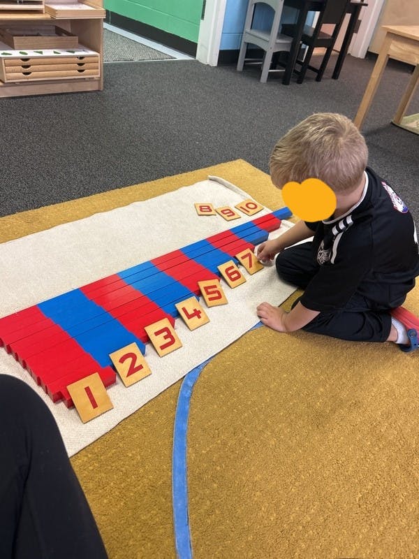 Child on floor playing with numbered wooden blocks and red and blue rods