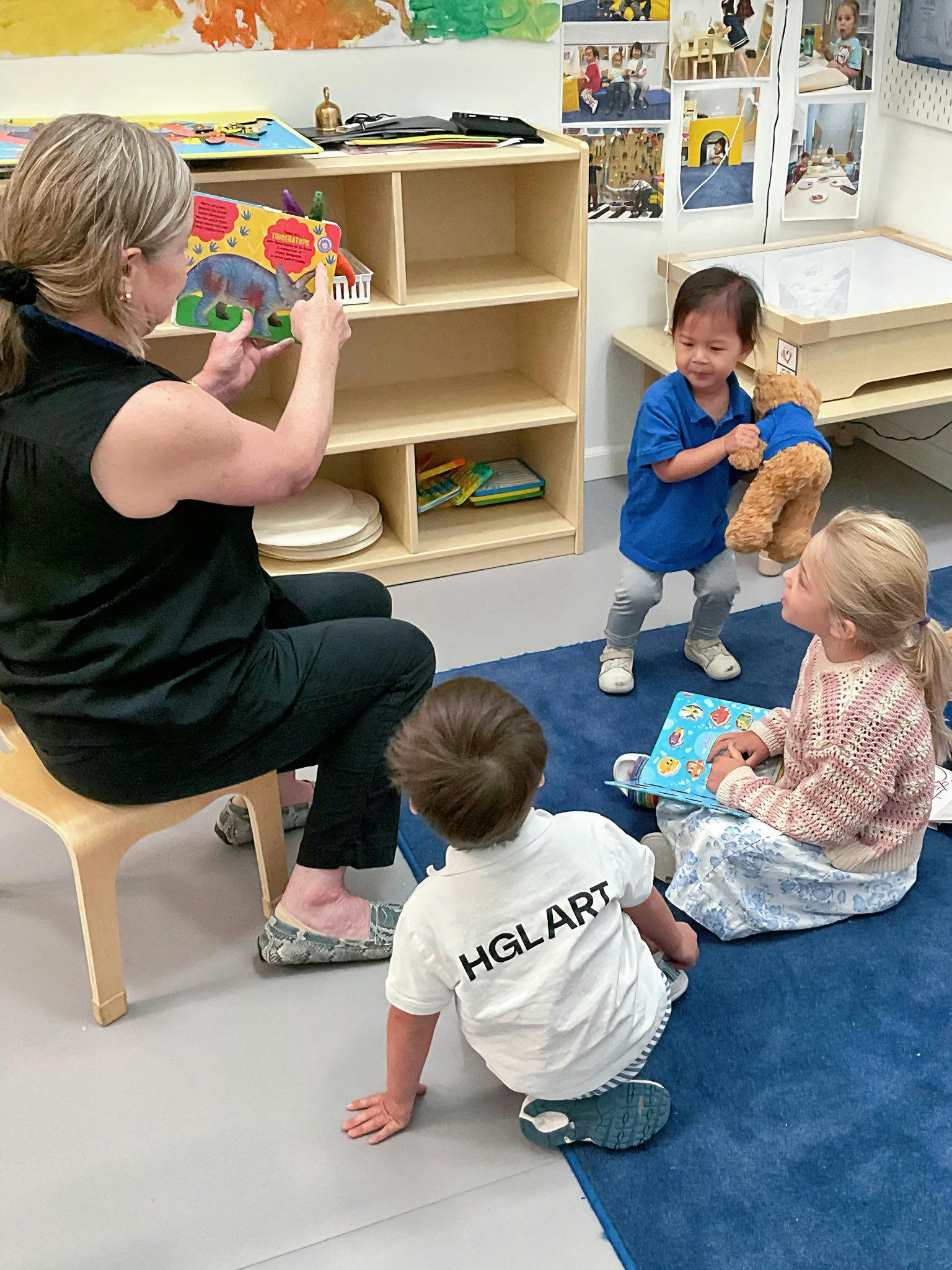 Adult reading a book to three children in a classroom