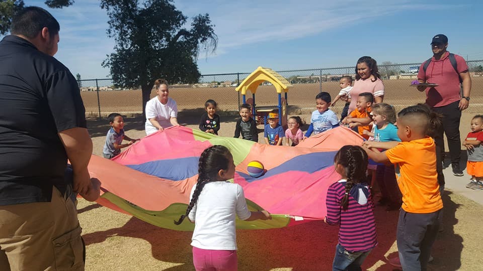 People and children playing with a colorful parachute outdoors