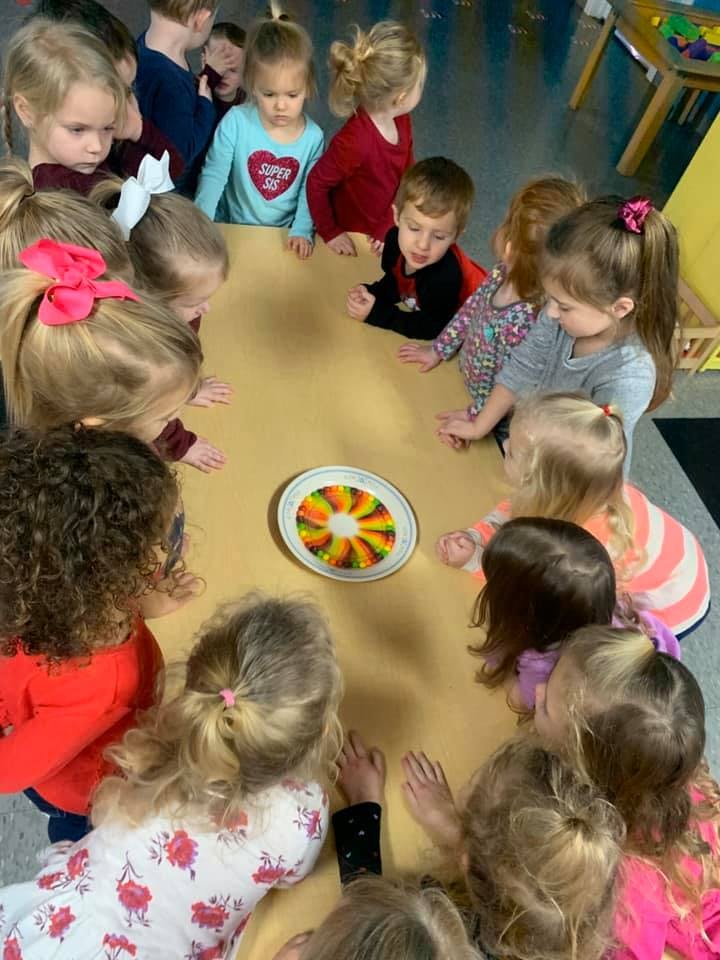 Children gathered around a table looking at a colorful plate