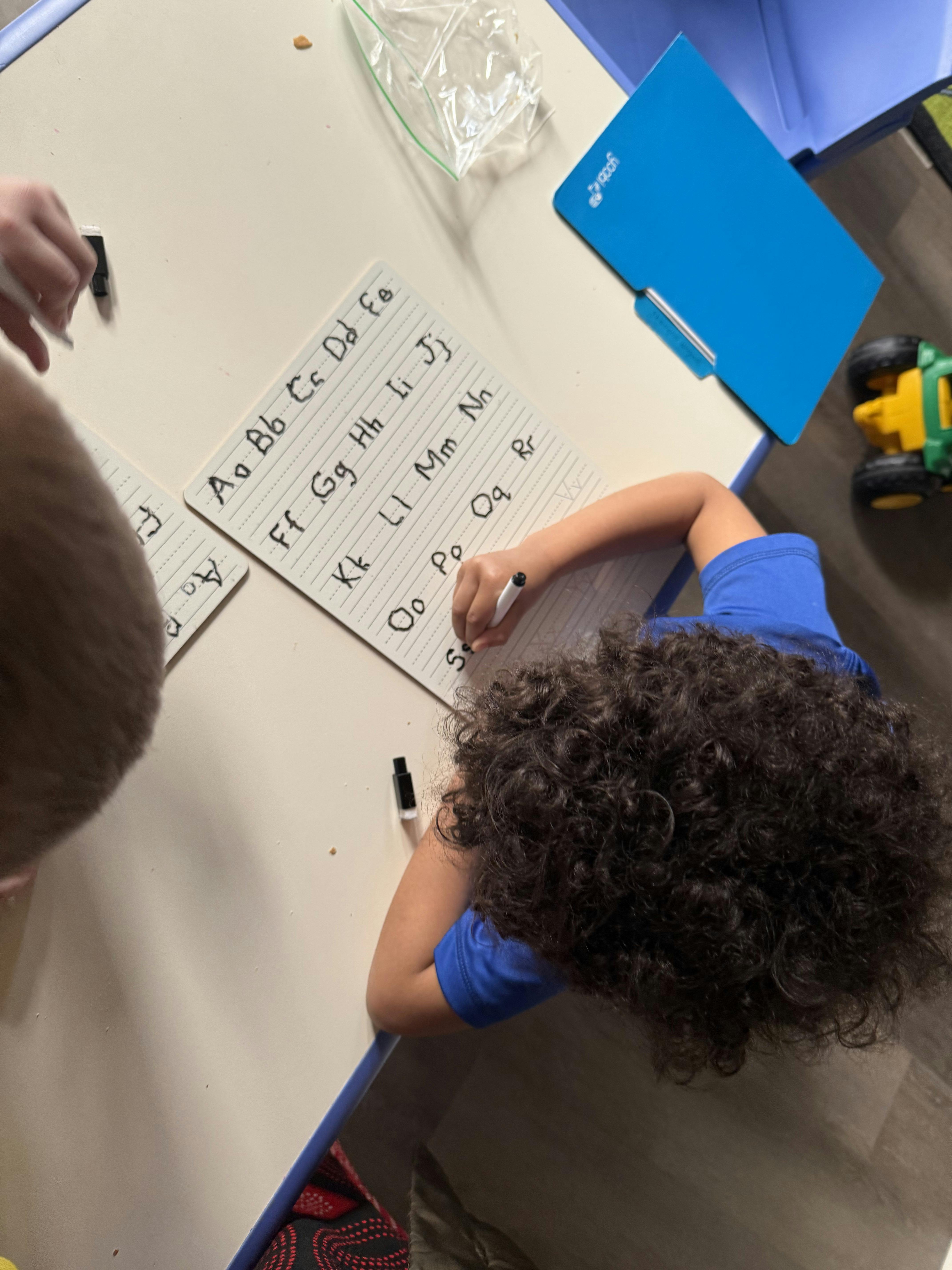 Child writing letters on a paper with an alphabet chart