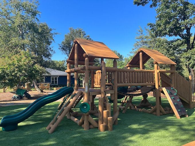 Wooden playground structure with a green slide and rock climbing wall