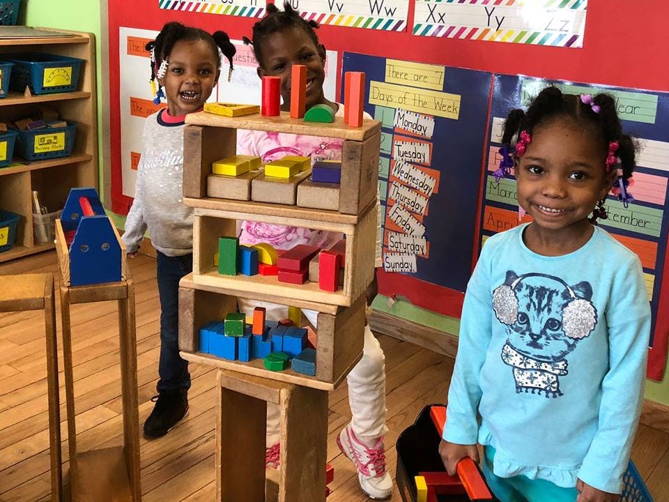 Three children playing with wooden blocks in a classroom