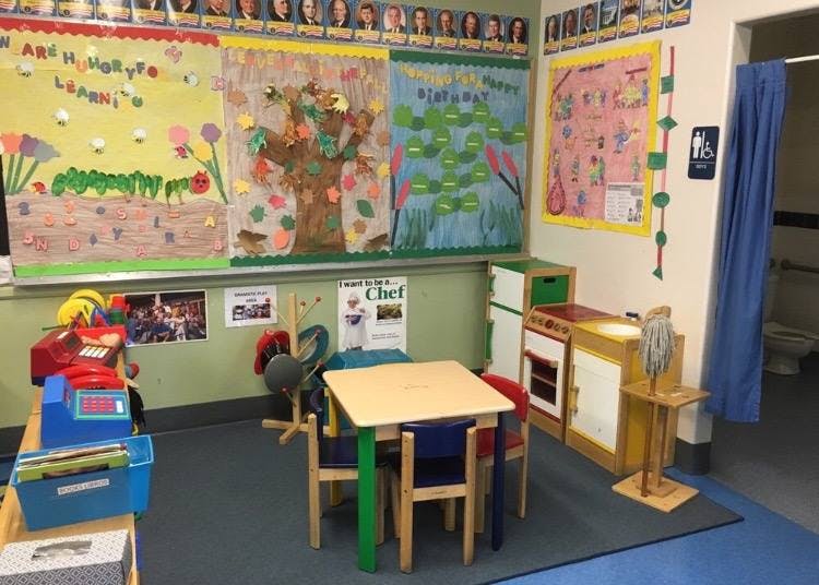 Classroom with children's artwork on walls, small table and chairs, and play kitchen