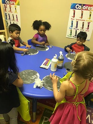 Children sitting at a table doing an art activity with paint