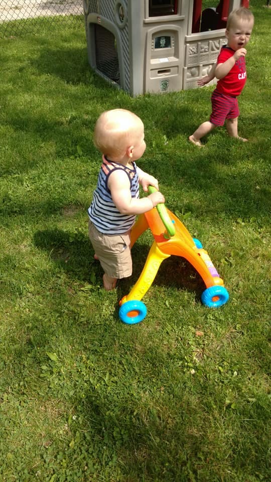 Child pushing a walker on grass with another child in background