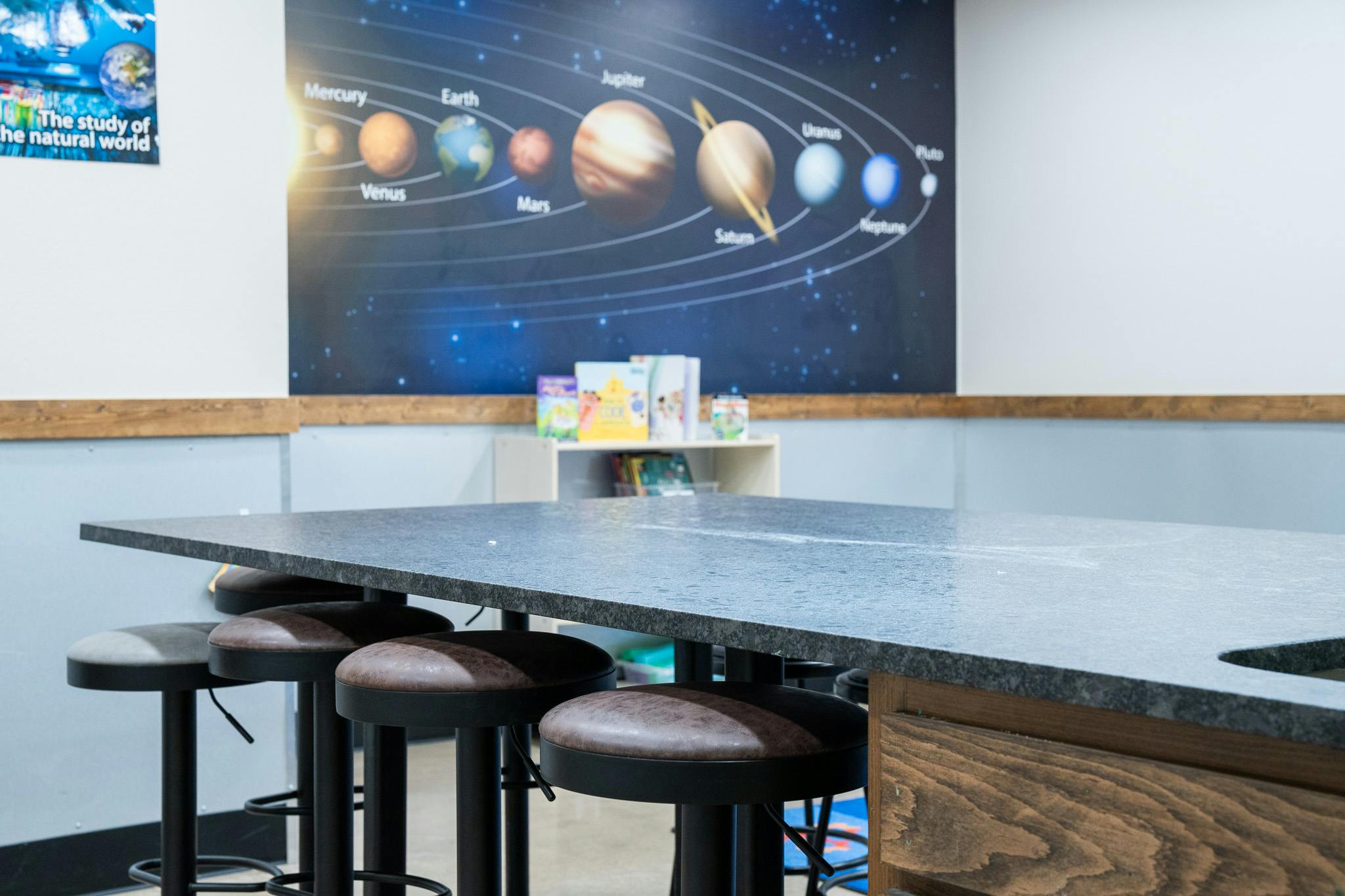 Classroom interior with a table and stools in front of a solar system wall decal