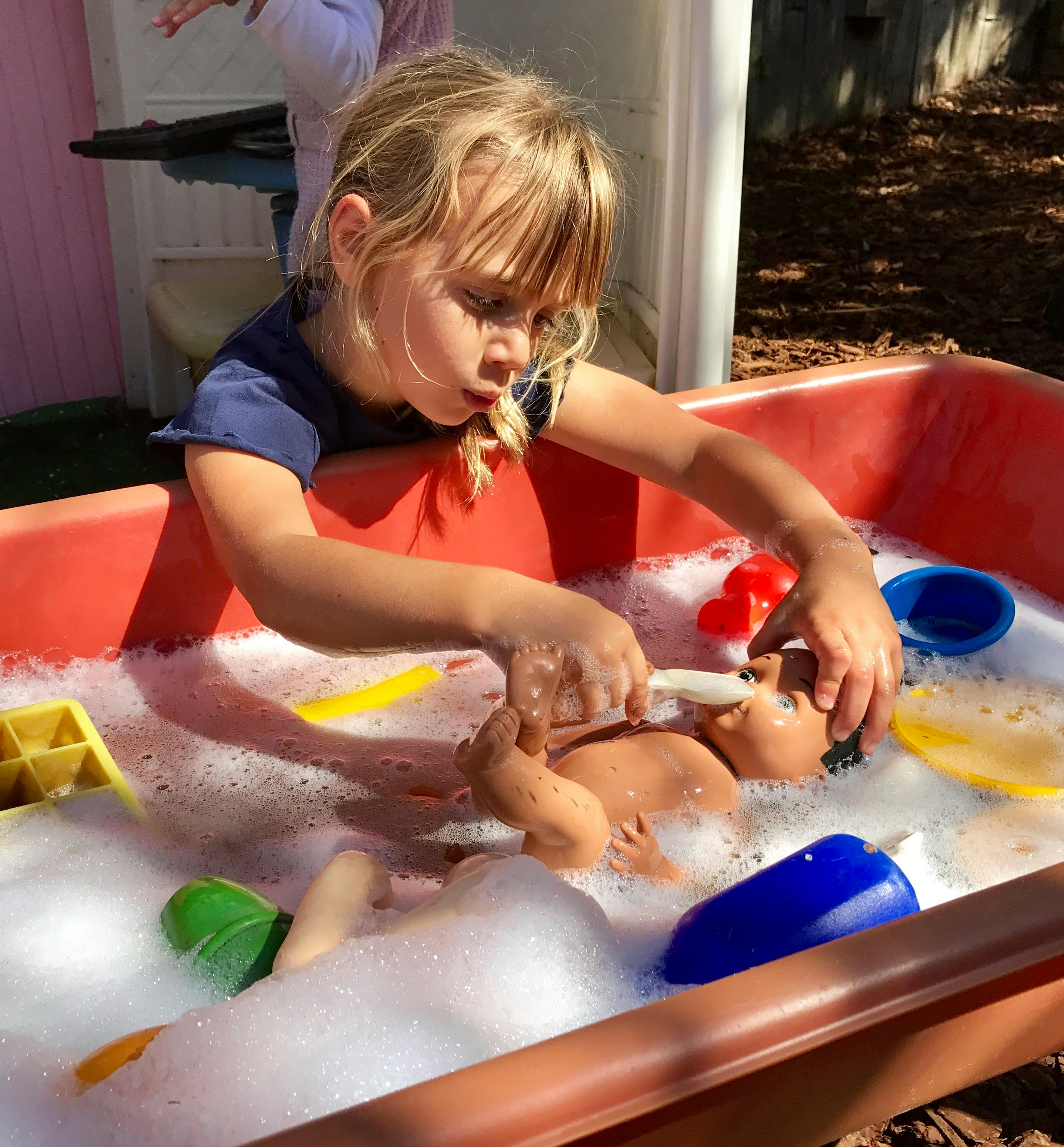 Child playing with a doll in a tub of soapy water