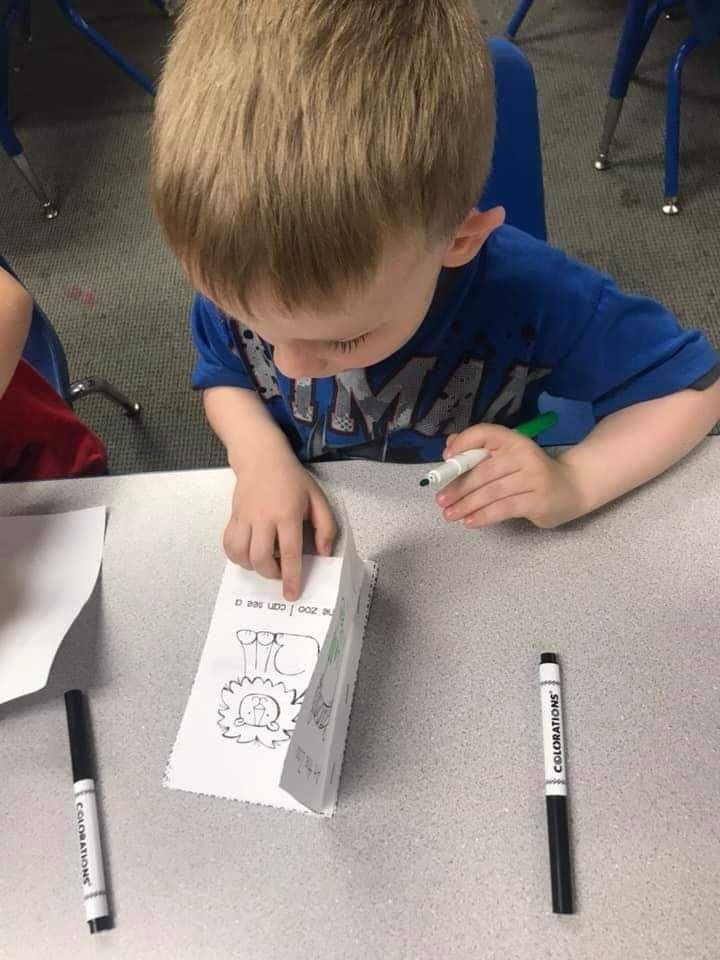 Child coloring a drawing on a paper bag with a marker