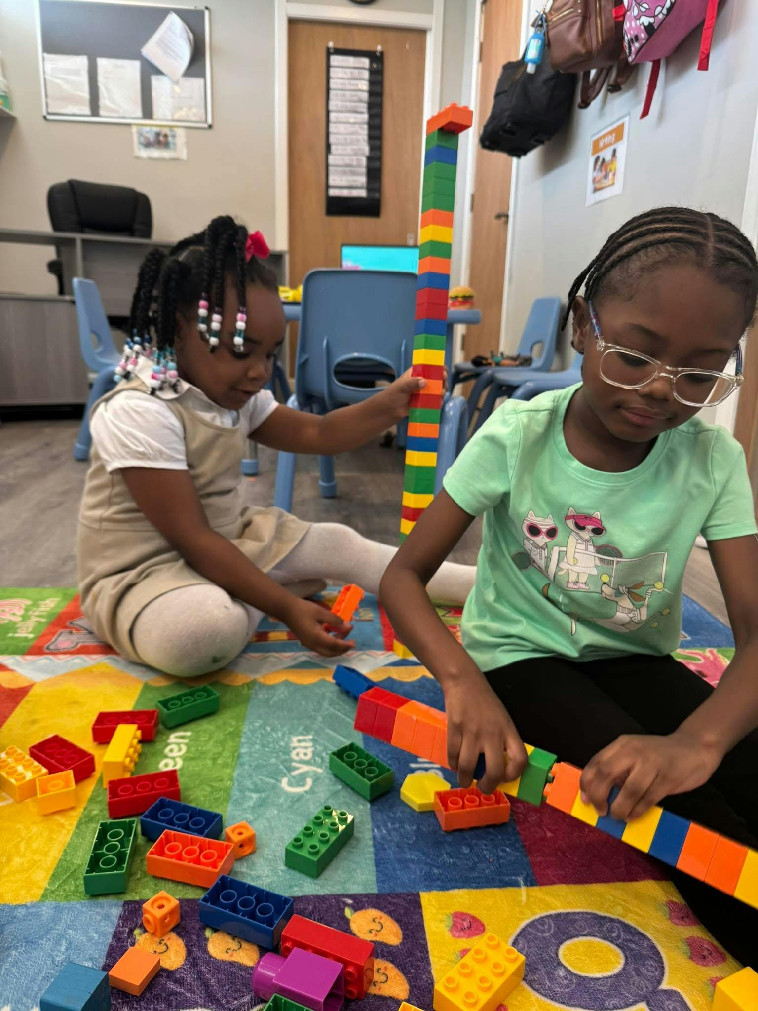 Two children sitting on a colorful floor rug stacking colorful plastic blocks