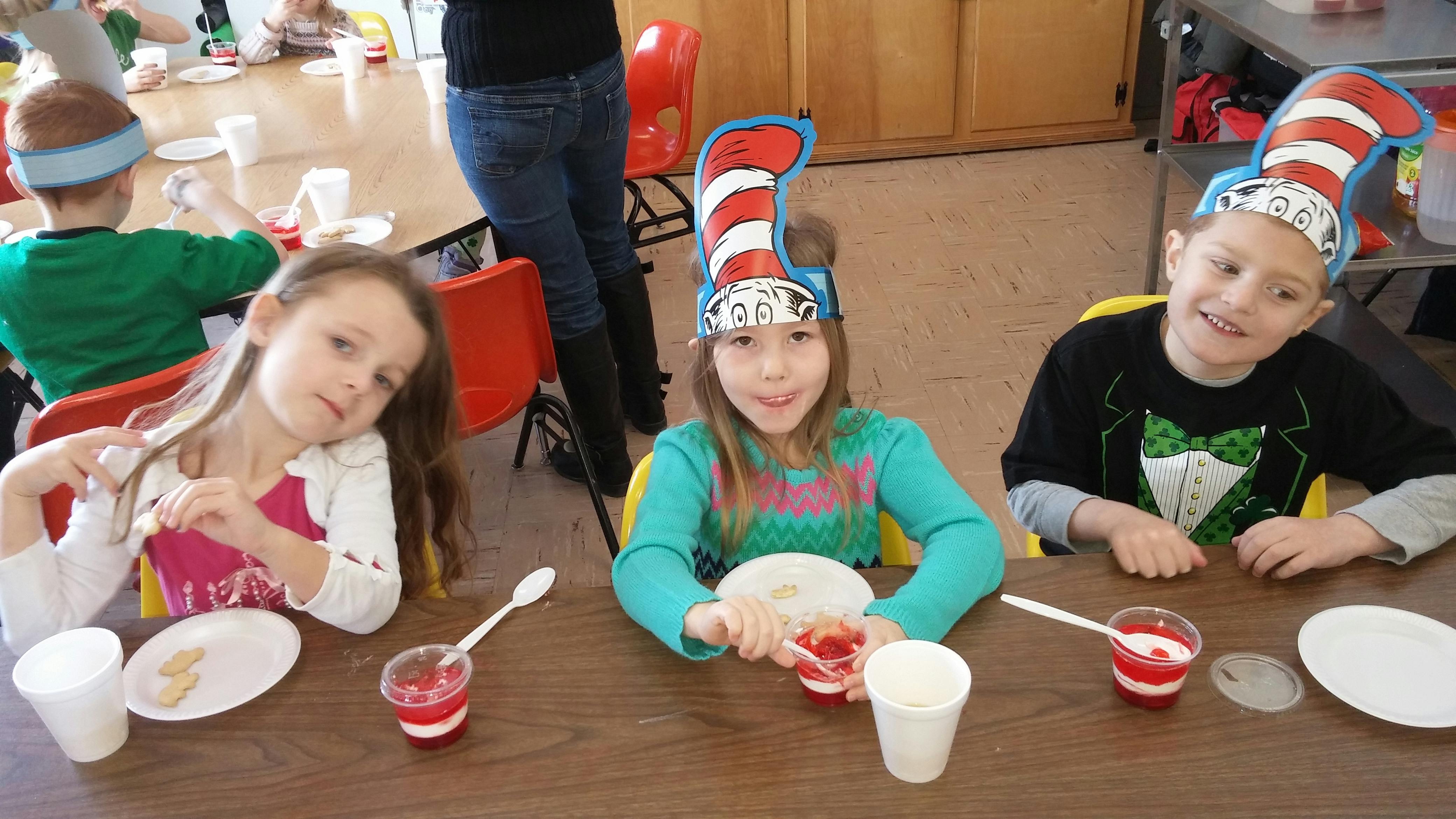 Three children at a table with desserts, two wearing striped hats
