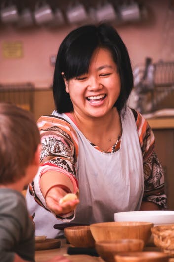 Person in an apron offering a small item to a child
