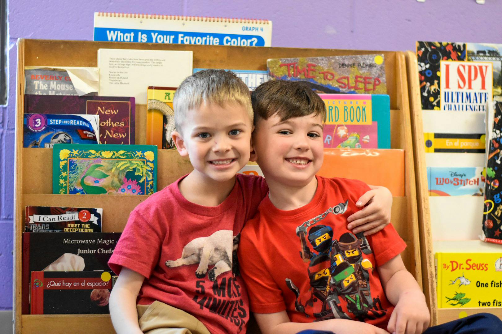 Two children smiling and embracing in front of a bookshelf with books