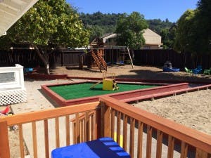 Outdoor play area with sandbox, green turf, and playground equipment