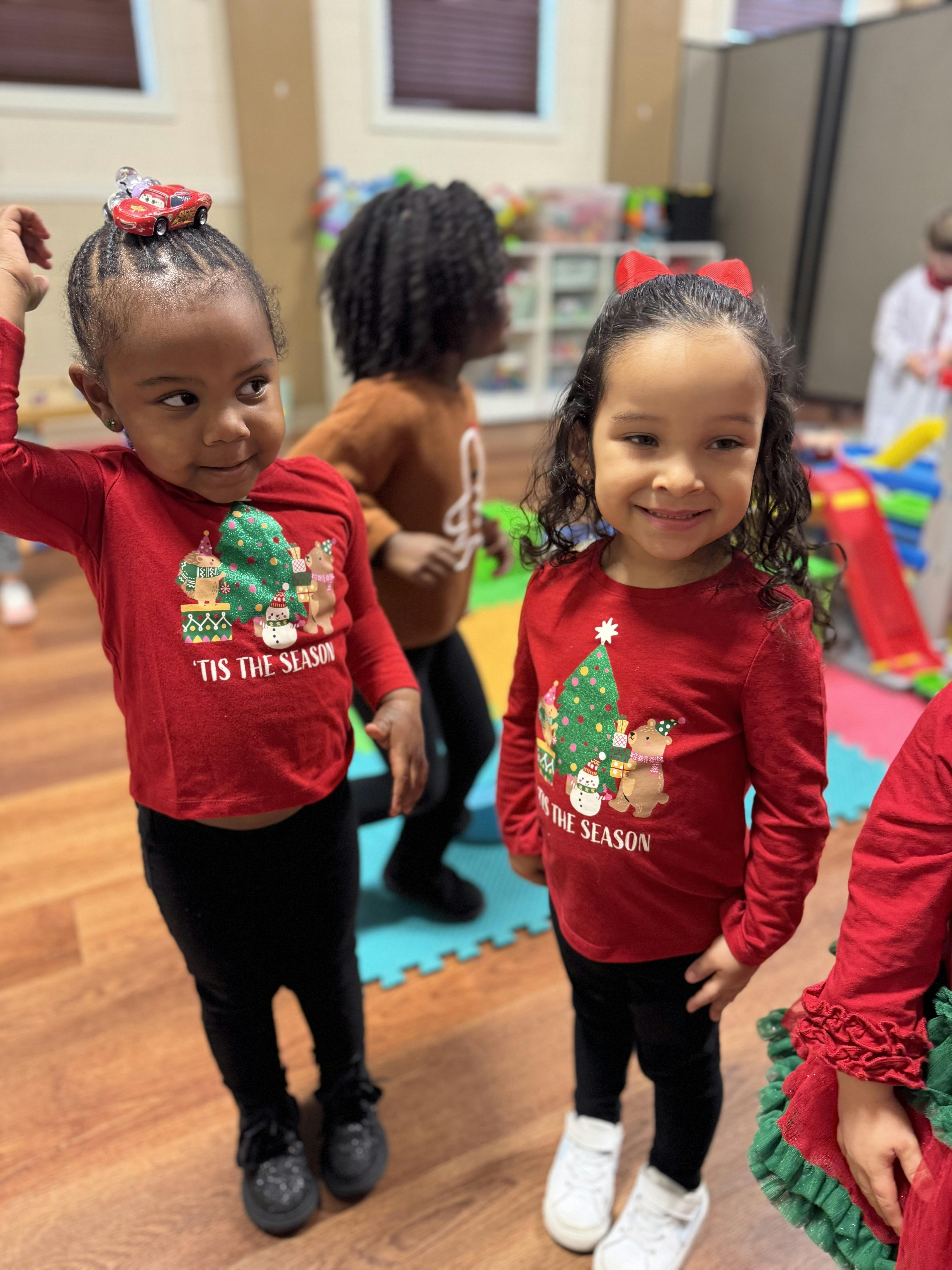 Three children in a playroom wearing holiday themed long sleeve shirts