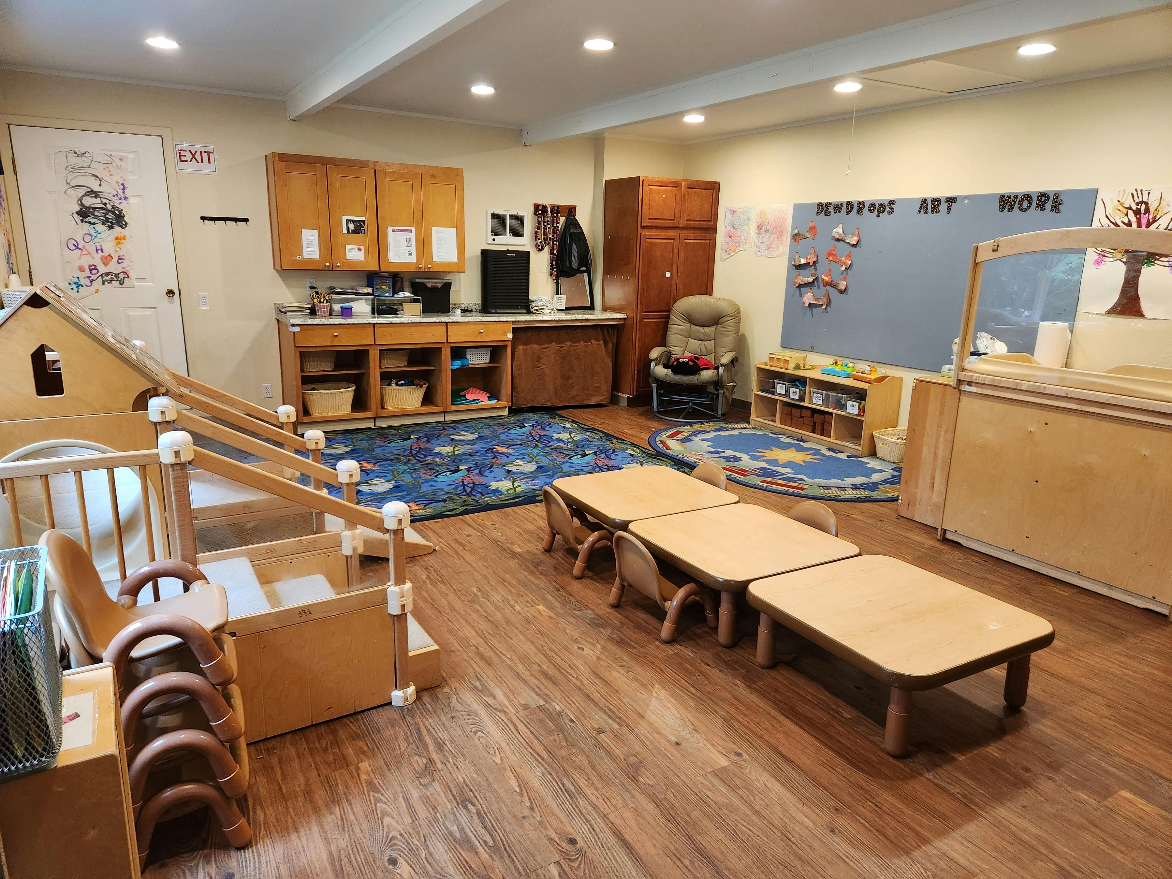 Classroom with small tables and chairs, play structures, and a chalkboard