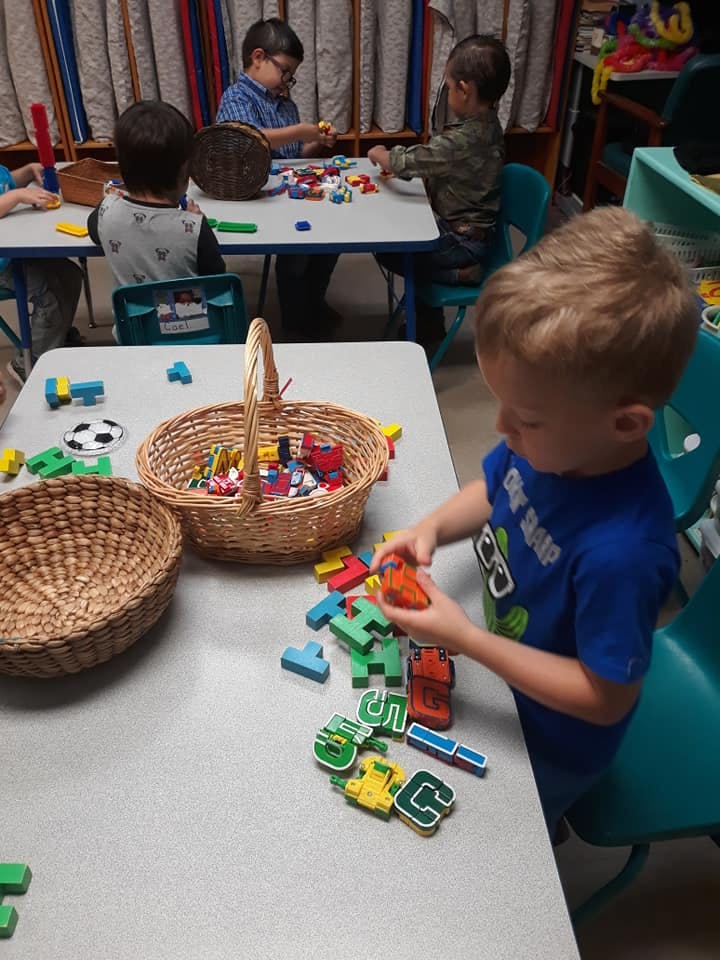 Children playing with blocks and toys at tables in a classroom