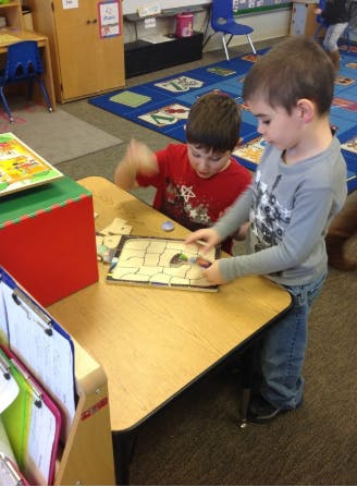Two children playing with a puzzle at a table in a classroom