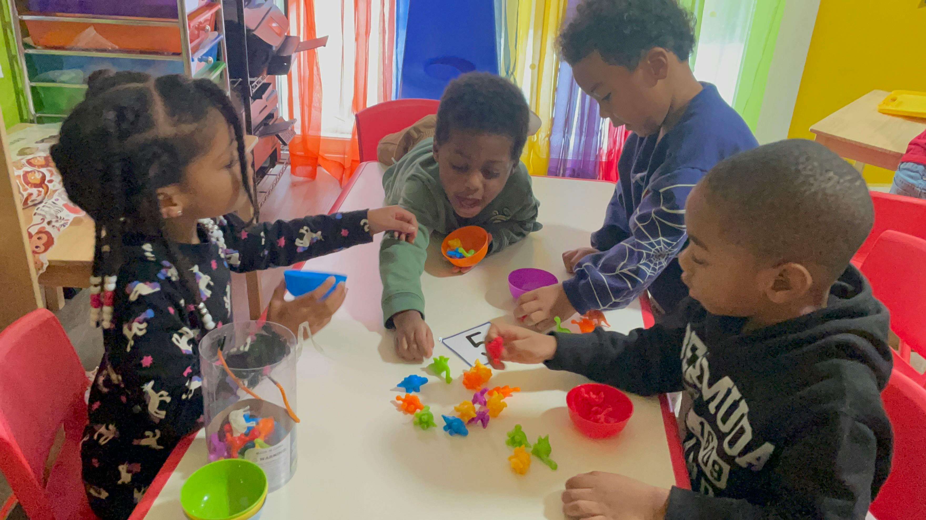 Four children at a table playing with colorful toy dinosaurs and cups