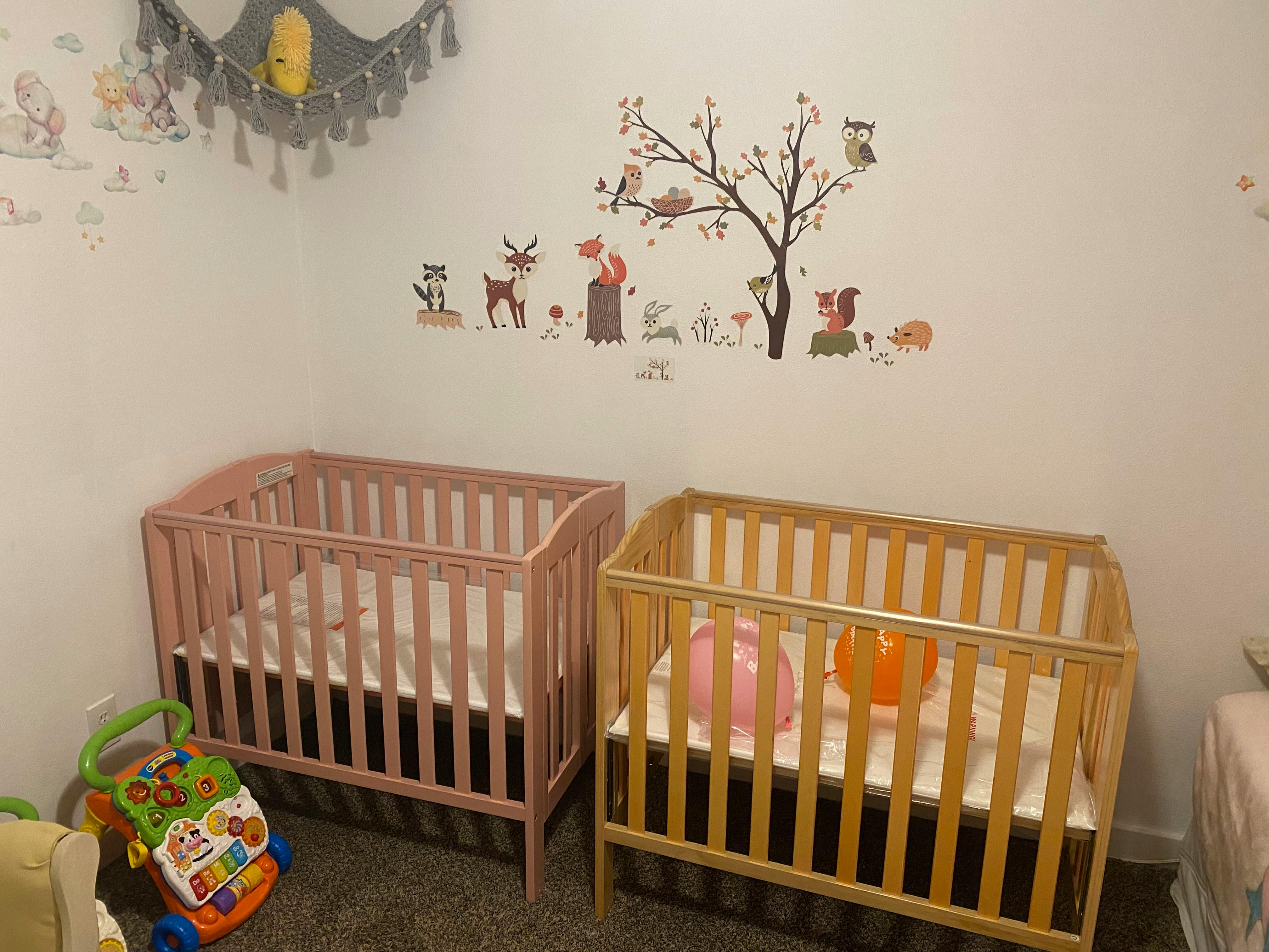 Two cribs in a room with wall decals
