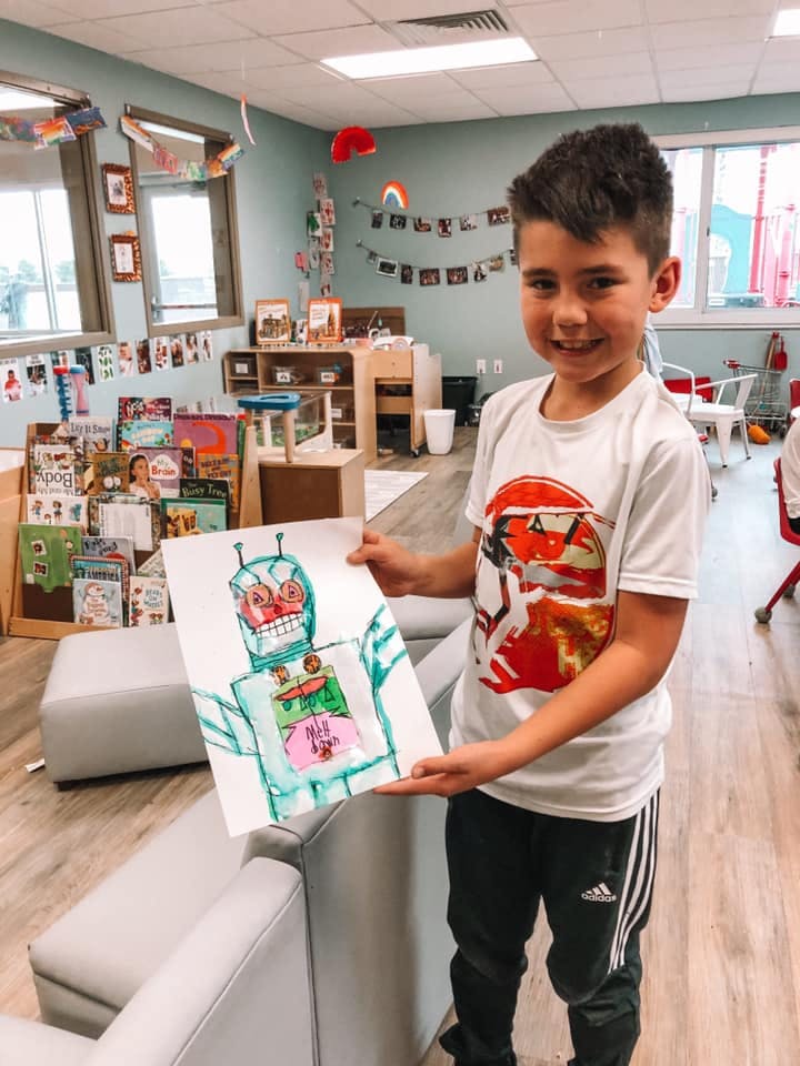 Child holding up a drawing of a robot in a classroom