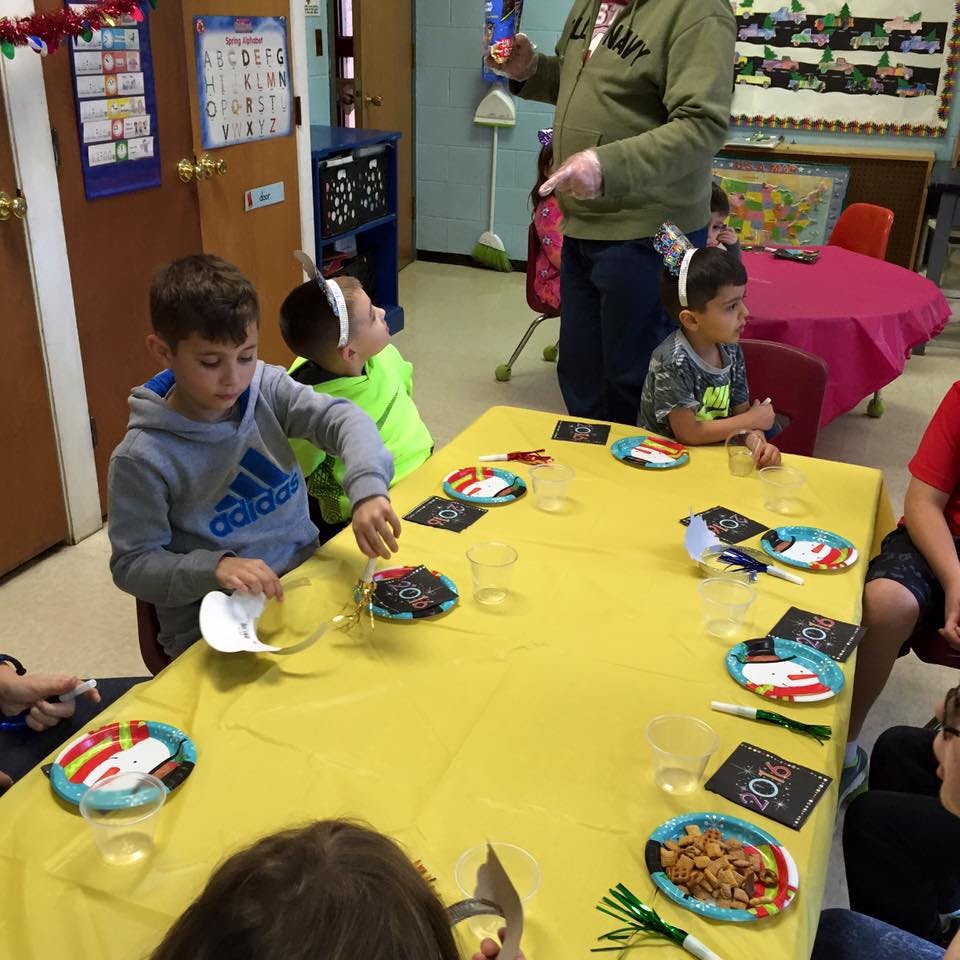 Adult standing near children seated at a table in a classroom