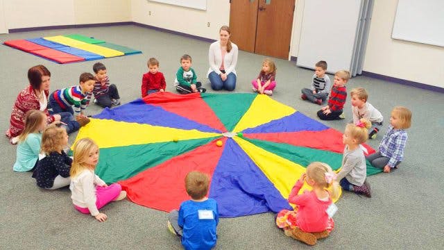 People and children sitting around a colorful parachute