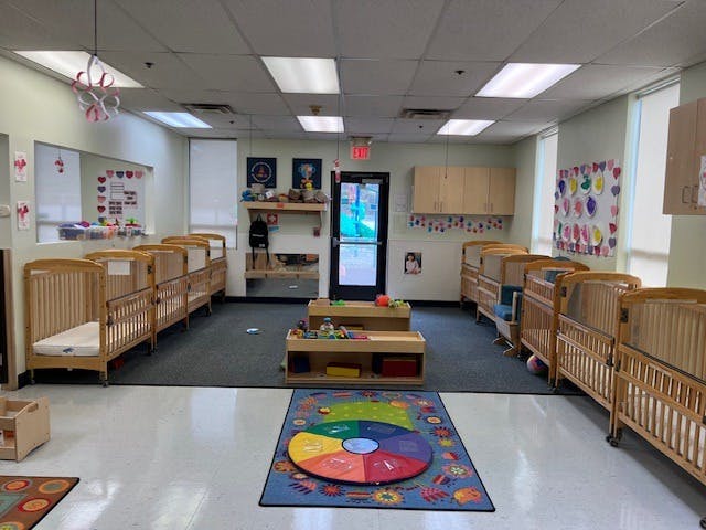 Rows of wooden cribs in a daycare room with a colorful play rug