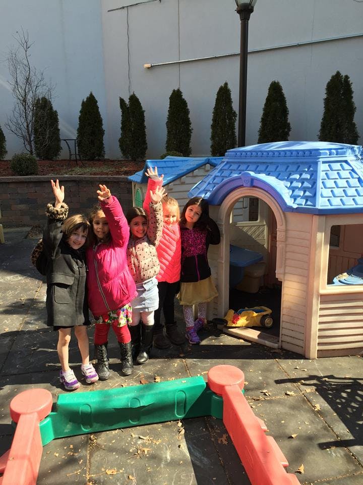 Children raising hands next to a playhouse