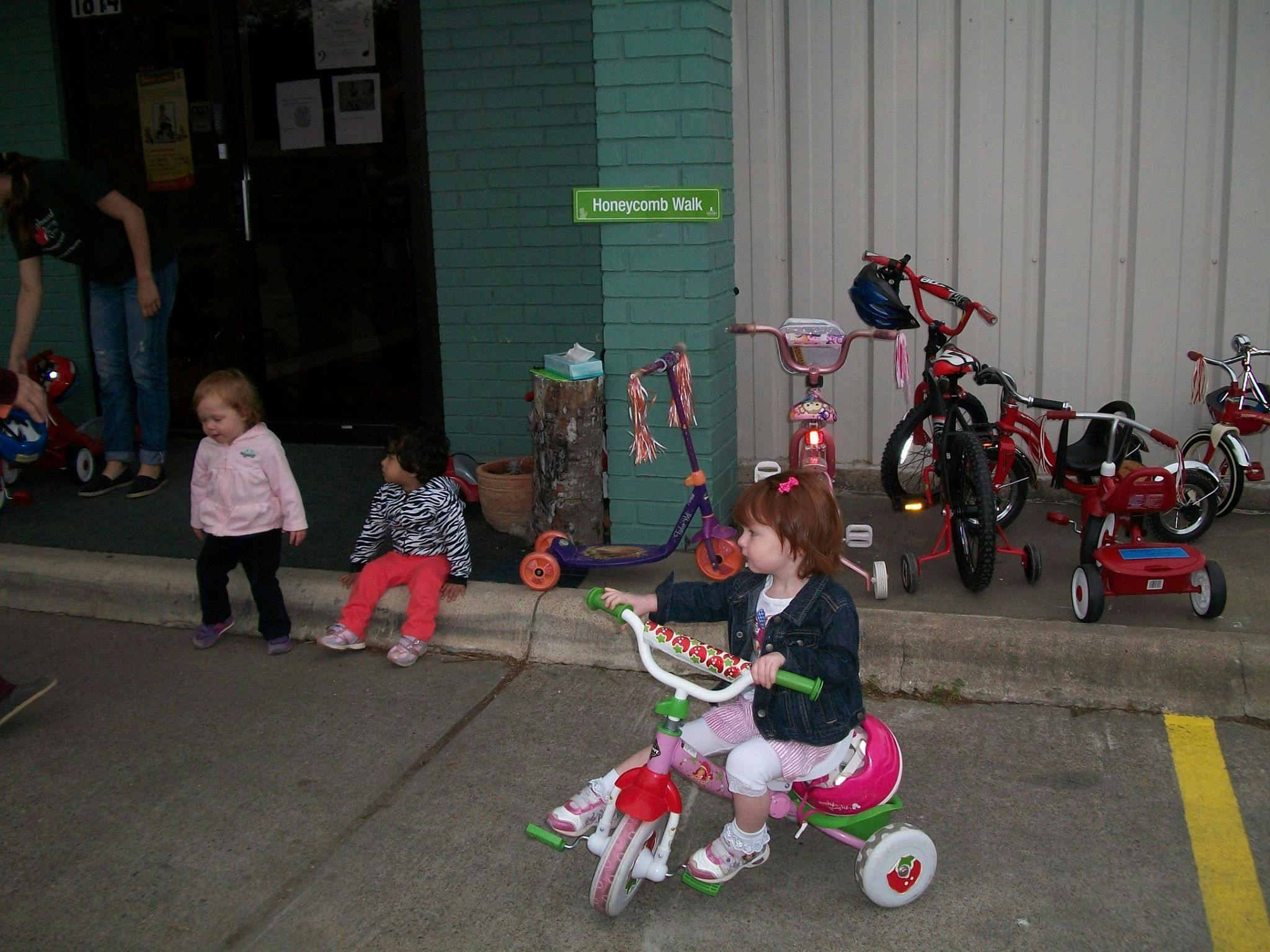 Child riding a tricycle with other children and bikes nearby