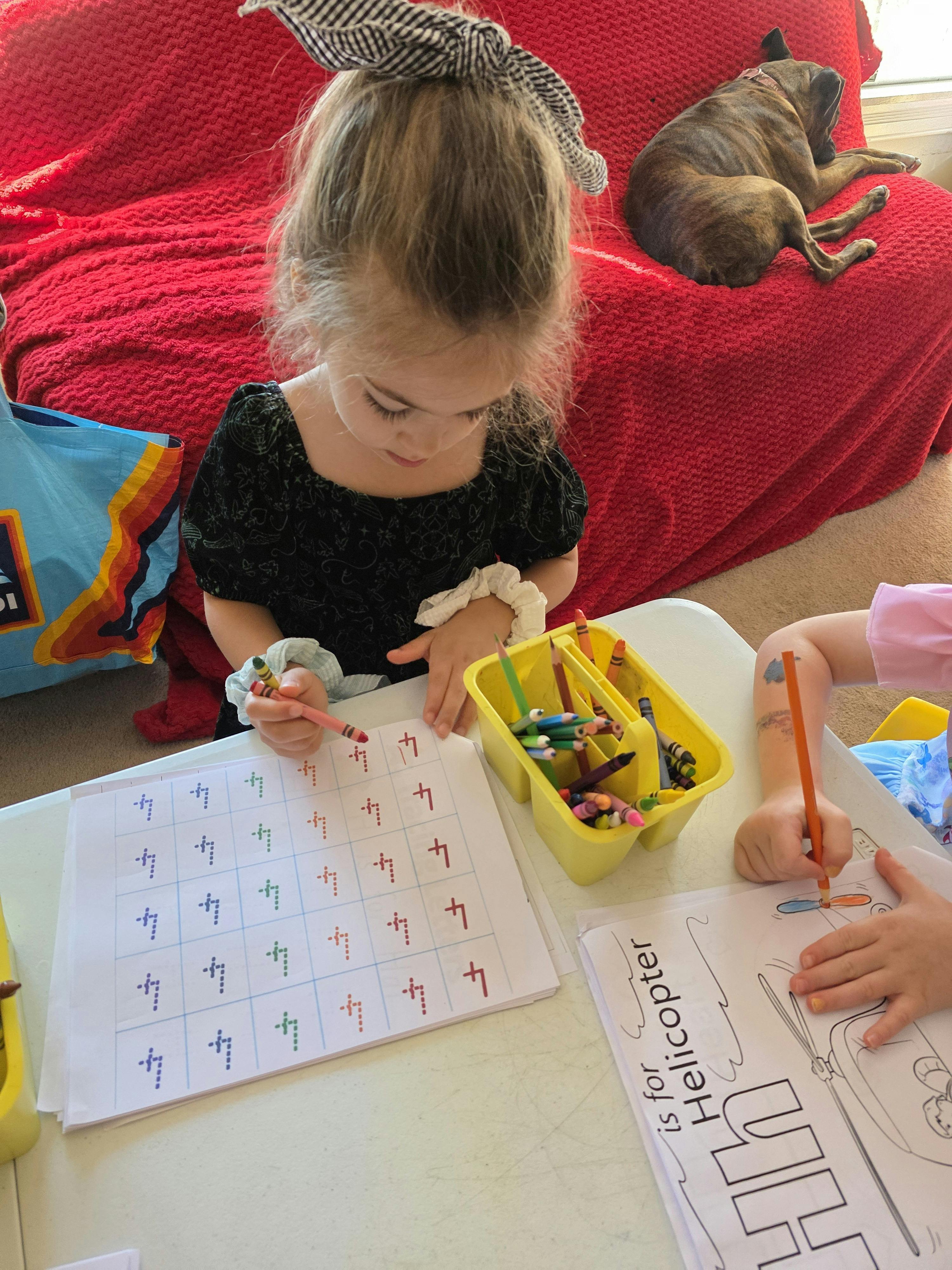 Two children coloring and tracing numbers on activity sheets at a table