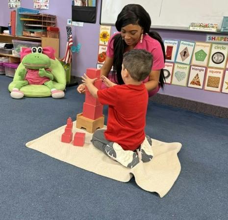 A person and a child building a tower with blocks in a classroom