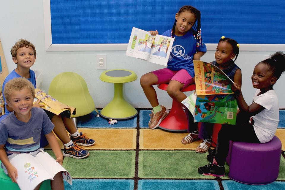 Four children and one teen sitting and reading books in a classroom