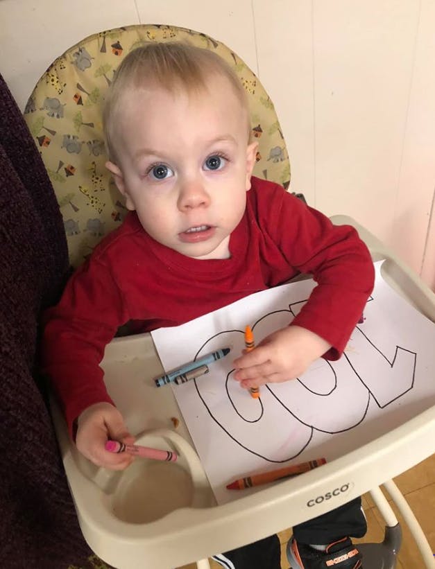 Child in a high chair with crayons and a coloring page
