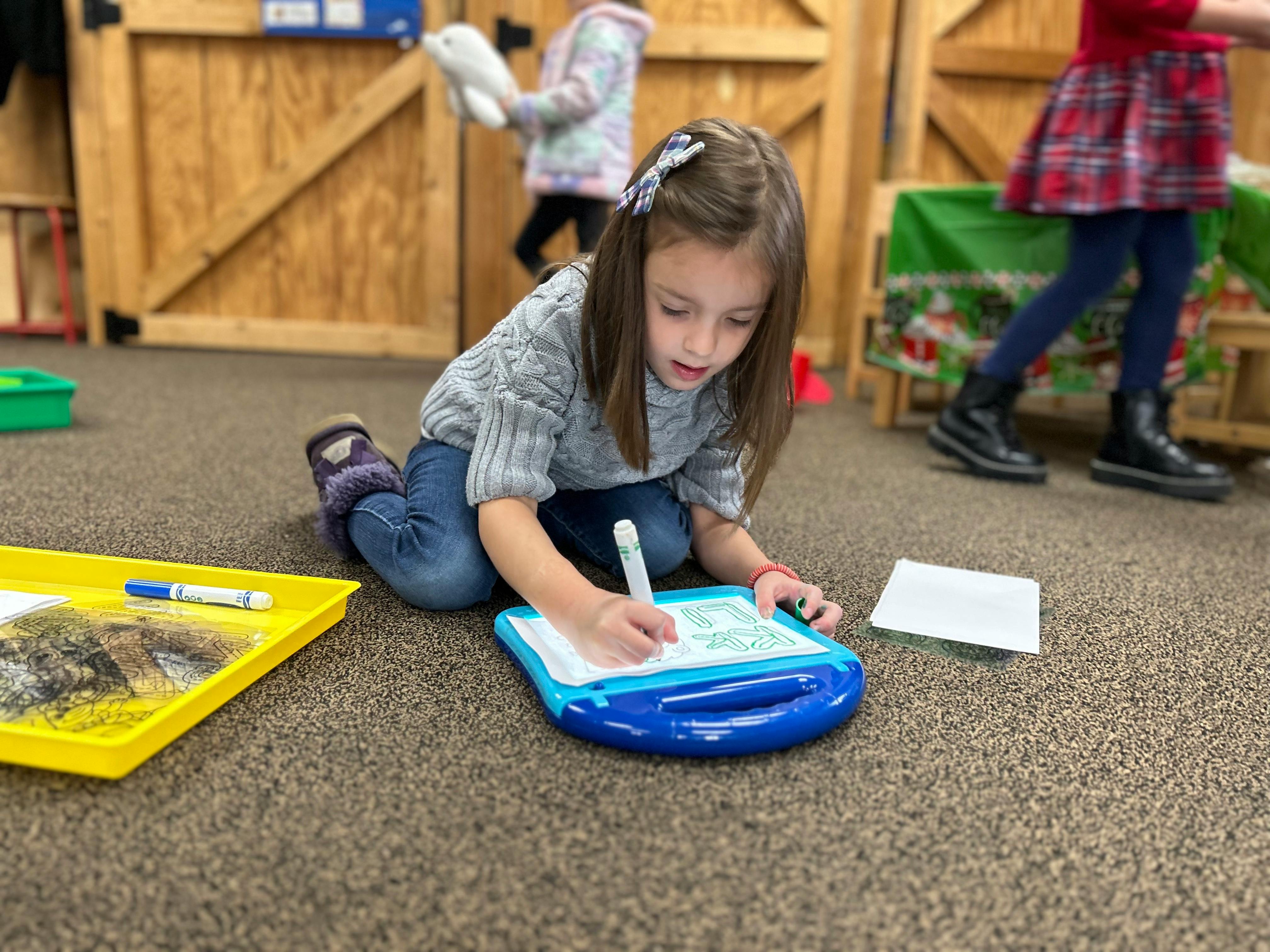 Child kneeling on floor drawing on a magnetic sketch pad