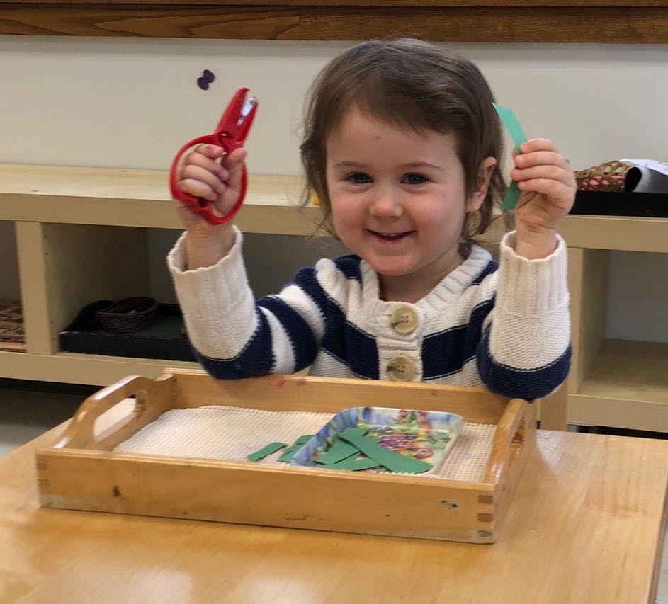 Child holding red scissors and green paper cutouts