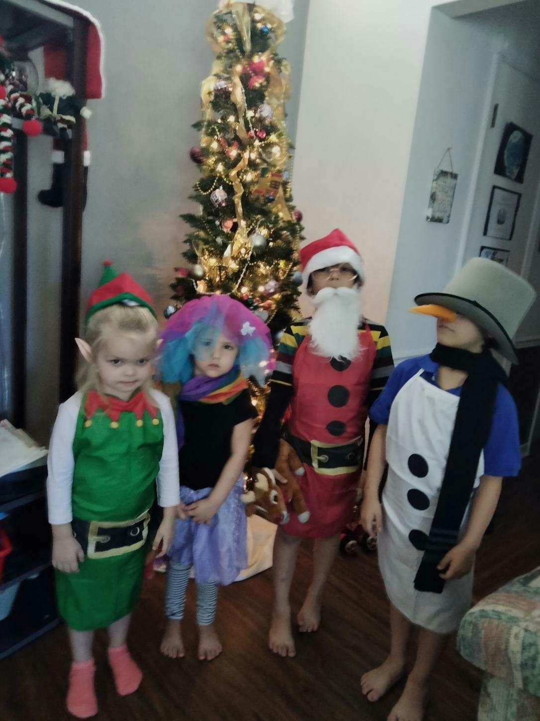 Four children in holiday costumes standing in front of a Christmas tree