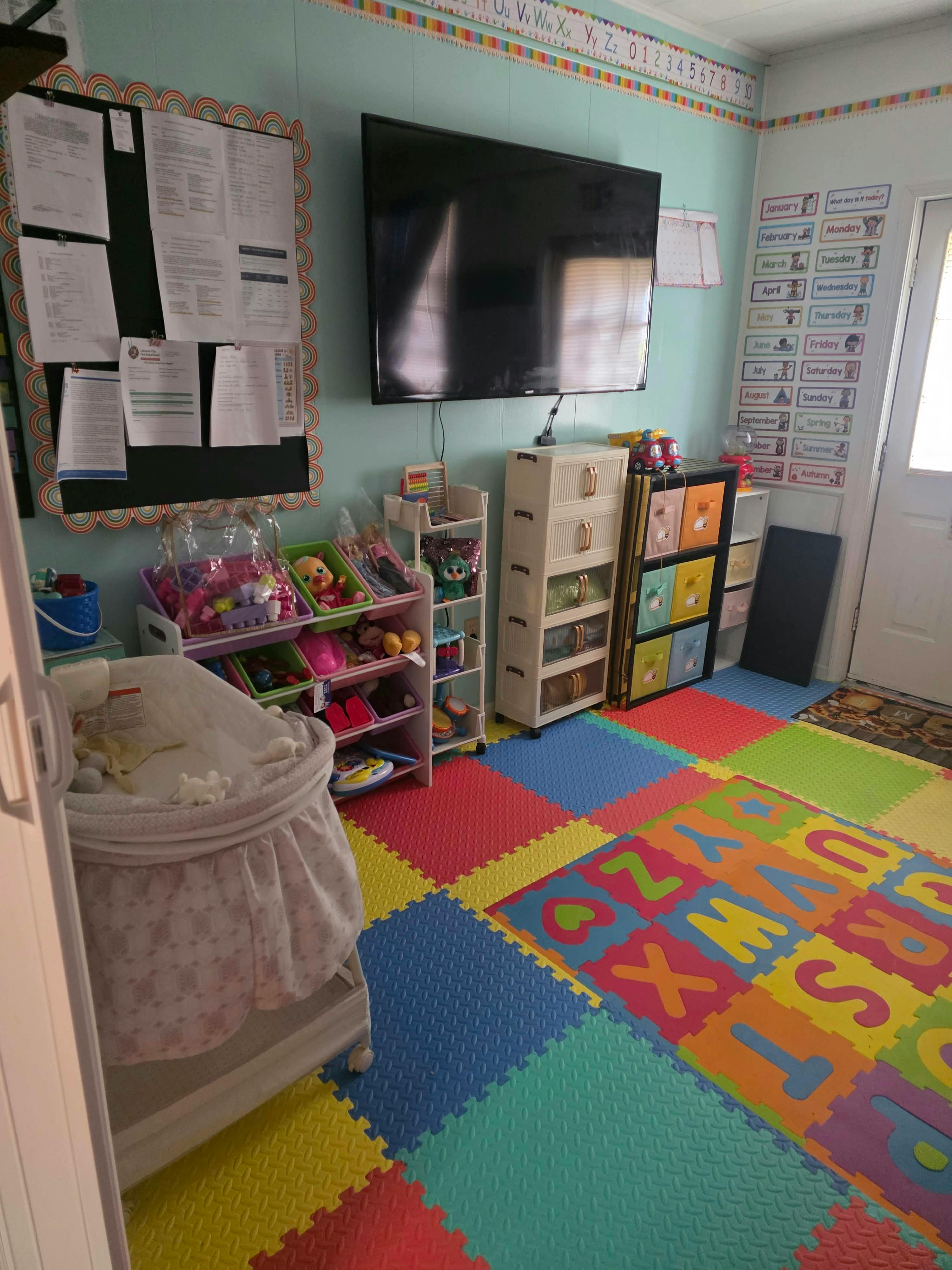Childcare room with alphabet floor mats, toy organizers, and a bassinet