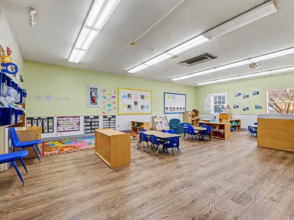 An empty classroom with small tables and chairs, toys, and learning materials